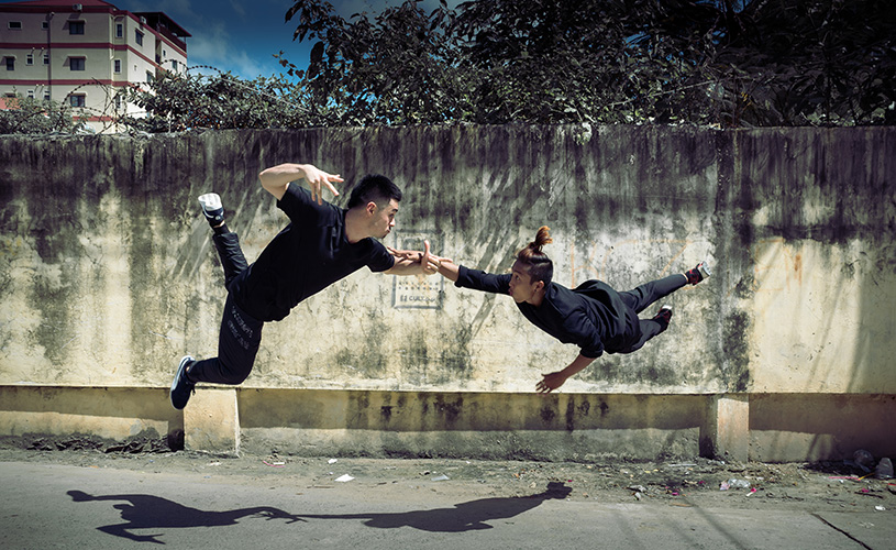 Two men are suspended in the air doing acrobatic dance in a carpark