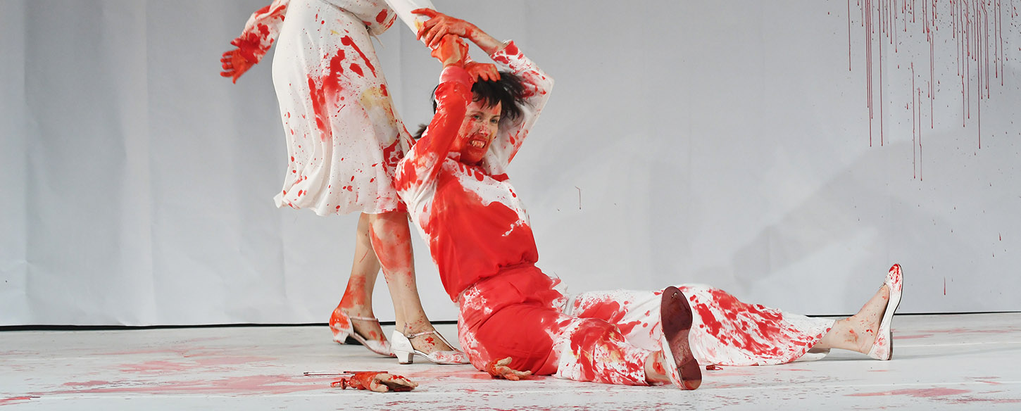 A women in a white suit covered in blood is being dragged across the floor