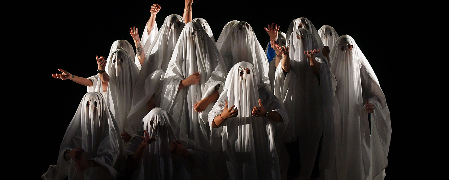 A large group of people are wearing sheets like ghosts with holes cut out for eyes