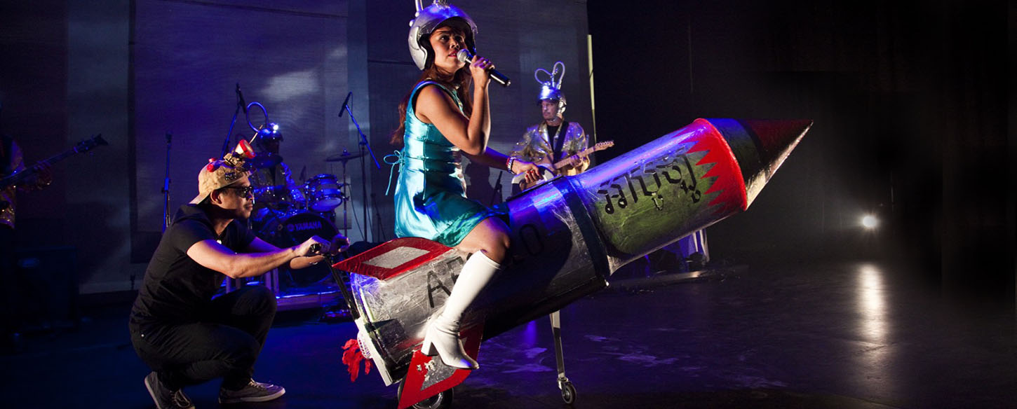 a woman is sitting on a rocket on stage singing