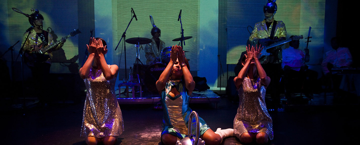 thee woman are centre stage kneeling with their hands in front of their faces