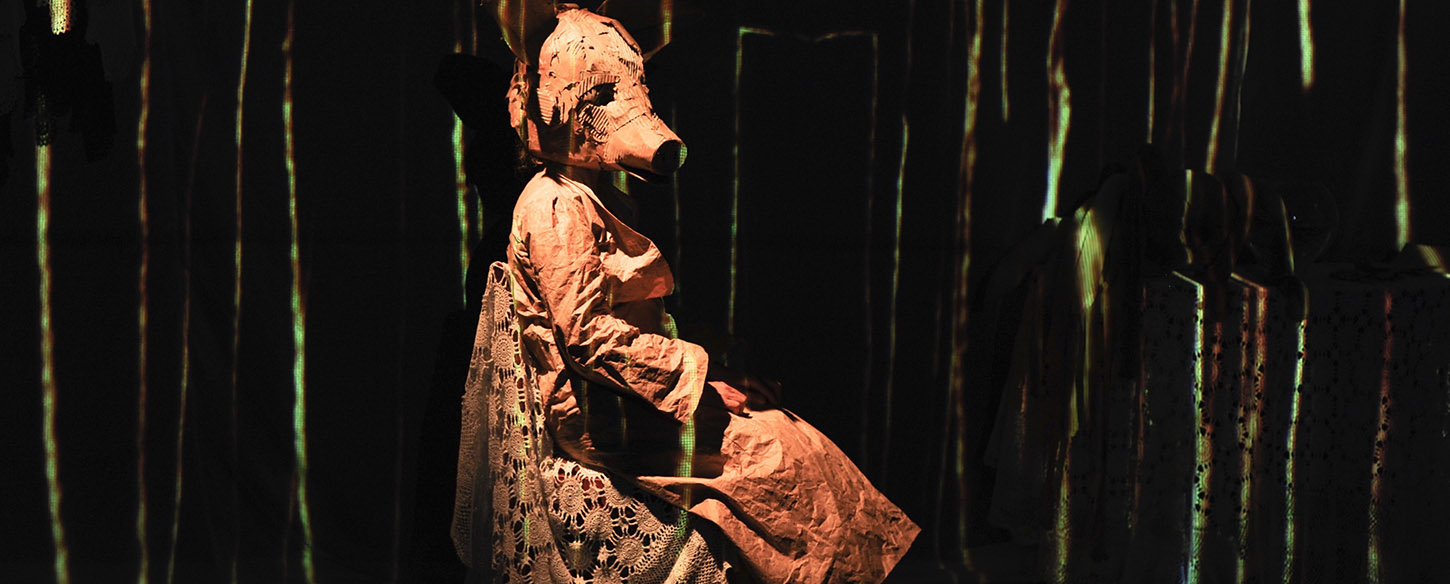 a woman sits on a chair in a white dress with a paper mache pig head