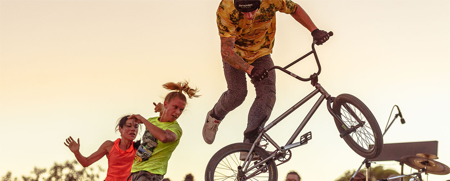 Young man on a bmx bike doing a trick in a skate park. there is a dancer behind him.