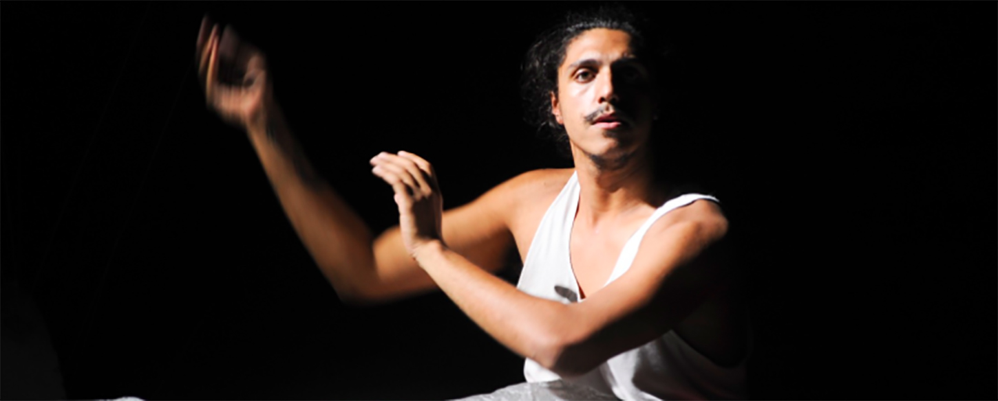 a young man in a white singlet holds his arms to the side sitting on stage